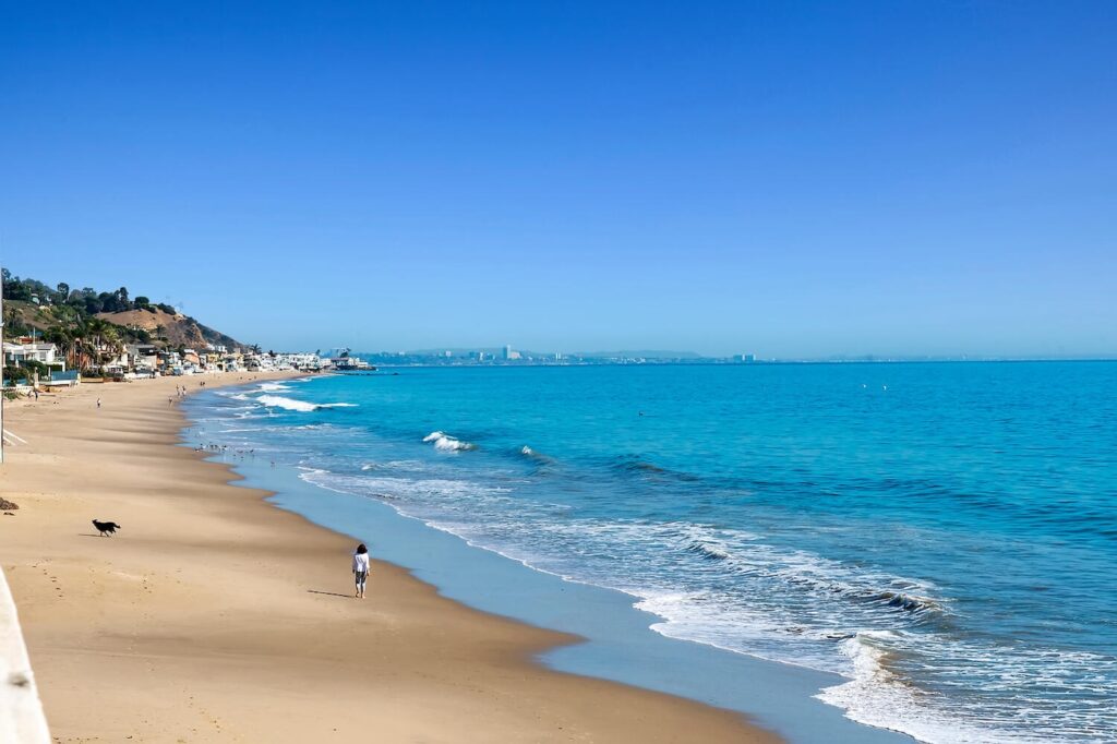 Wide view of Carbon Beach in Malibu with shoreline, ocean waves, and beachgoers on a clear day