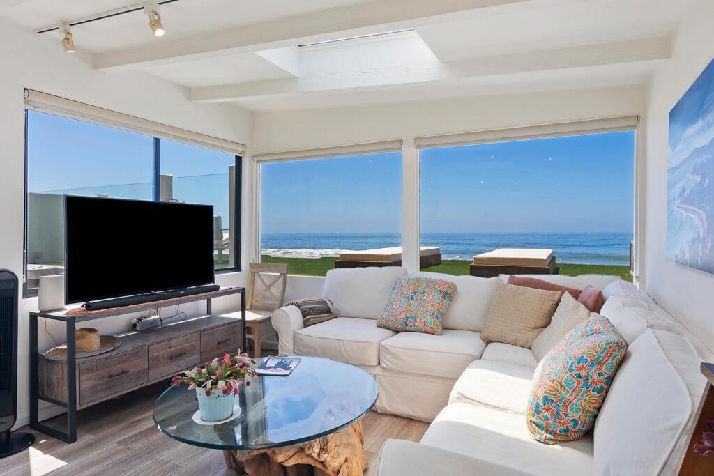 Bright oceanfront living room on Malibu Road with large windows, coastal decor, and panoramic views of the Pacific.