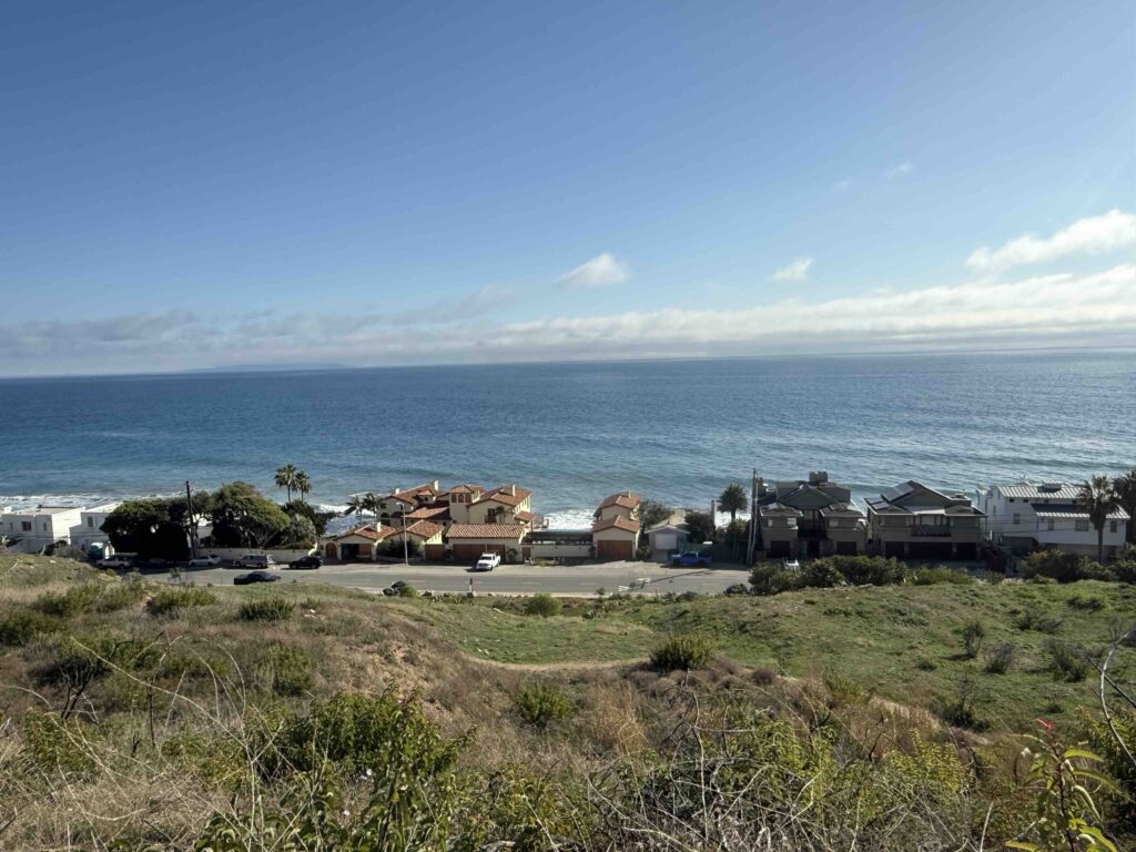 Elevated view of Malibu Road’s beachfront homes and coastal landscape on a clear morning.