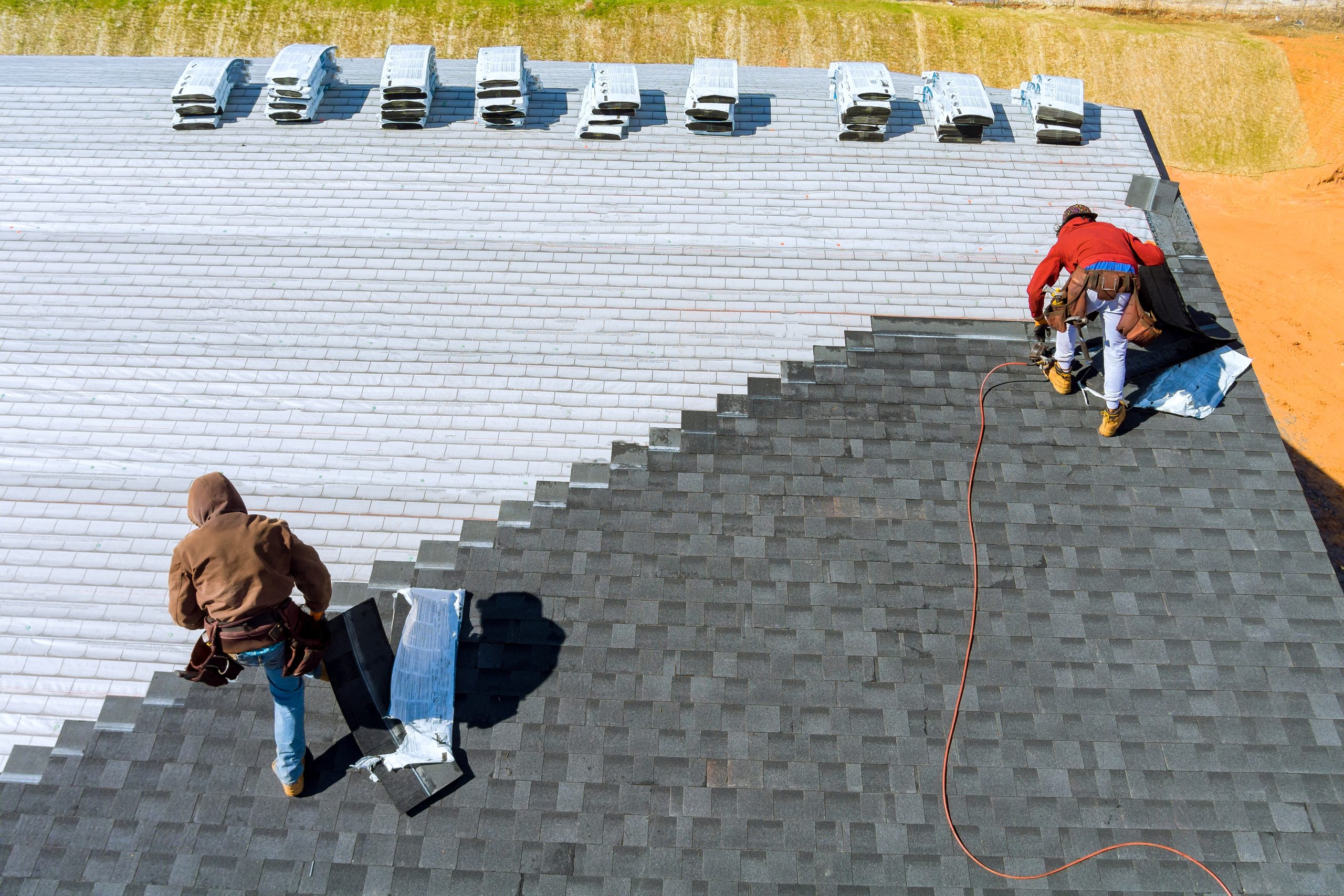 Aerial view in worker hands installing roof shingles with air hammer and nail