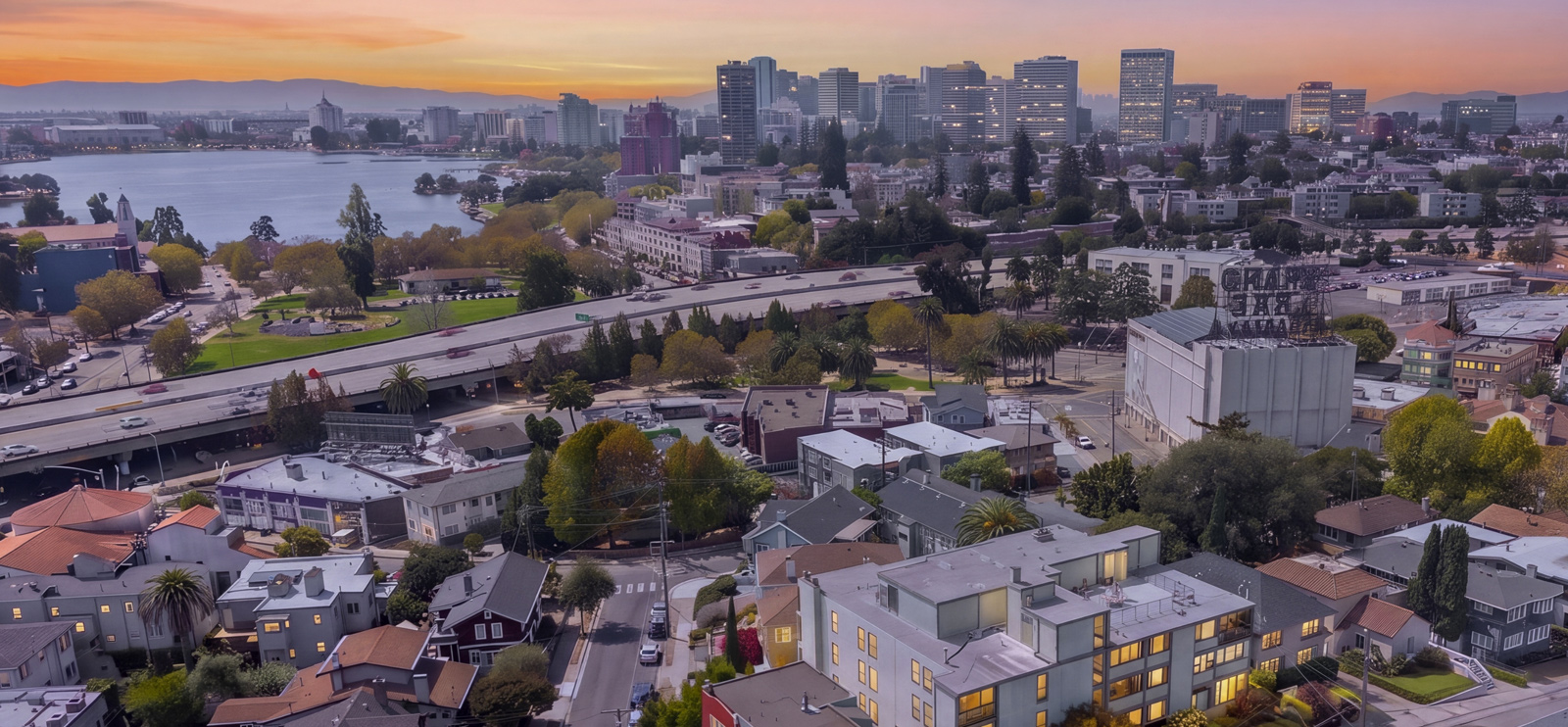 Aerial view at sunset over Oakland’s Grand Lake neighborhood, with the Grand Lake Theatre rooftop sign, Lake Merritt and the downtown skyline