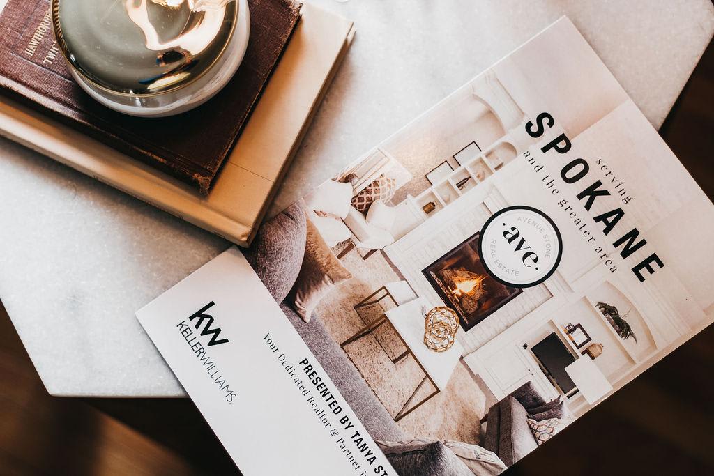 A stylish real estate brochure on a marble table, featuring a cozy living room image and a decorative candle.