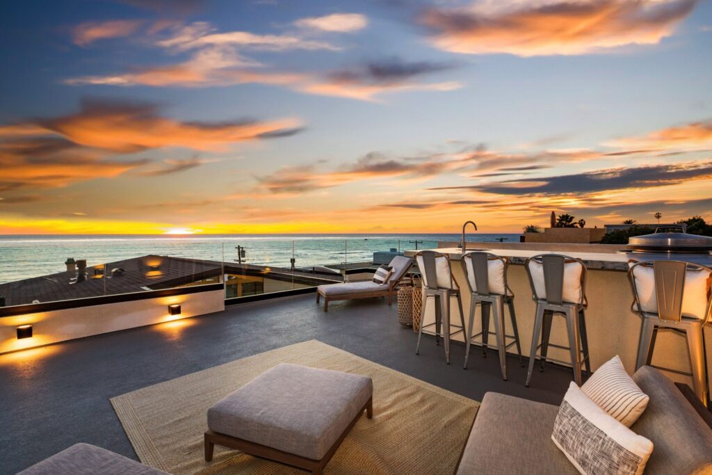 A second-level outdoor patio with kitchen and lounge chairs, overlooking the La Jolla coast at sunset.