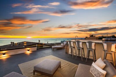 A second-level outdoor patio with kitchen and lounge chairs, overlooking the La Jolla coast at sunset.