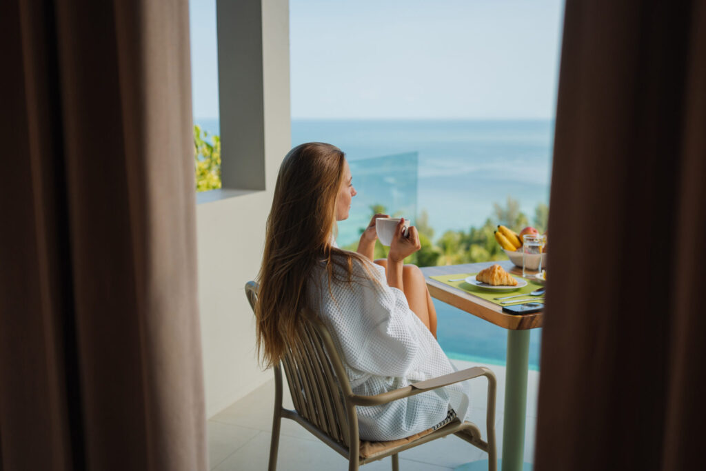 Relaxed woman enjoying breakfast and coffee on a private terrace overlooking a serene ocean view.