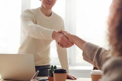 Two people shaking hands across a desk after a successful real estate negotiation, symbolizing a completed agreement.