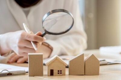 Real estate professional analyzing miniature house models with a magnifying glass, symbolizing home value assessment in 2025.