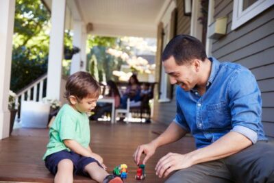 Father and son playing with toy cars on the front porch of their home, symbolizing family life and homeownership in the DMV area.