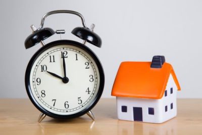 Clock beside a small house model symbolizing more time for homebuyers in 2025 housing market.