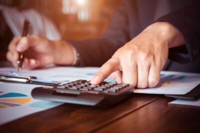 Close-up of a person using a calculator and financial charts to compare renting versus selling a home.